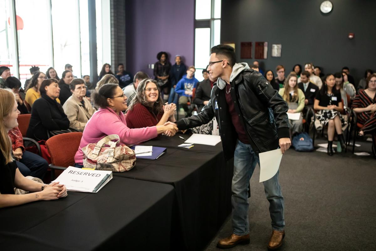 Young person shakes hand with judges in a crowded room