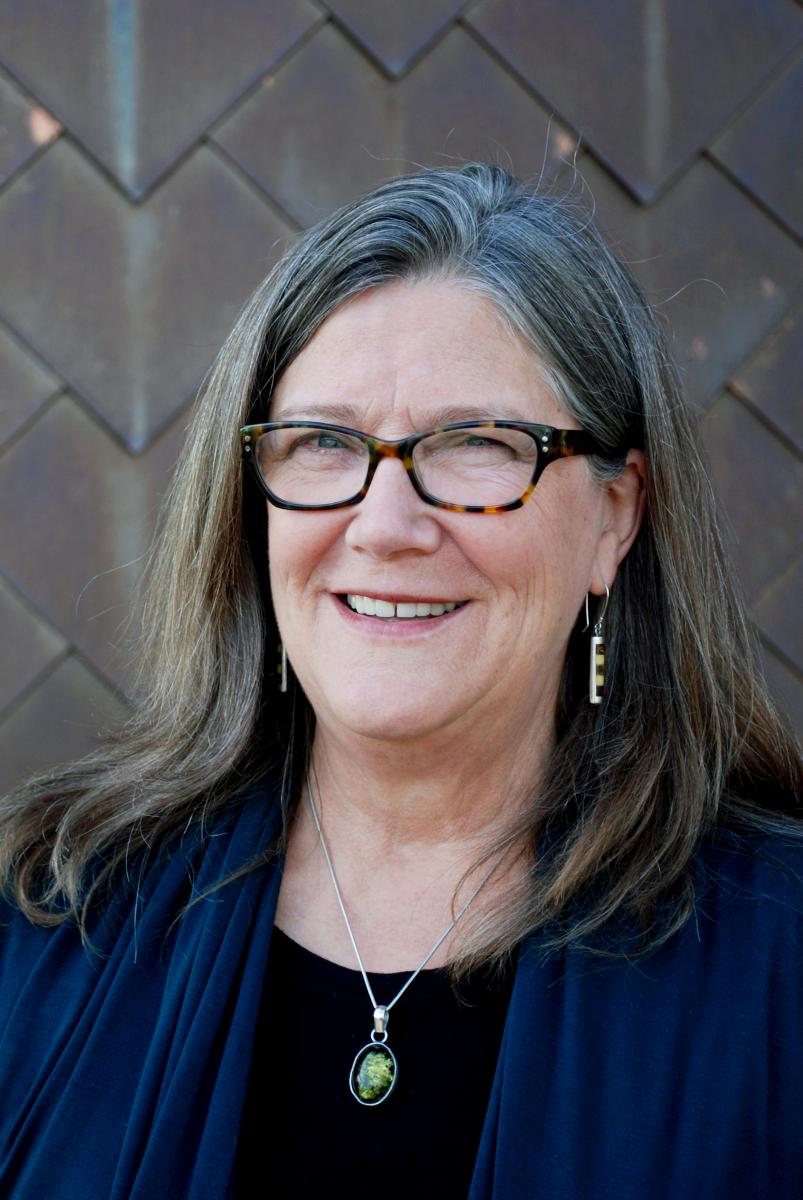 Alison Hawthorne Deming smiles in front of a concrete wall at the Poetry Center