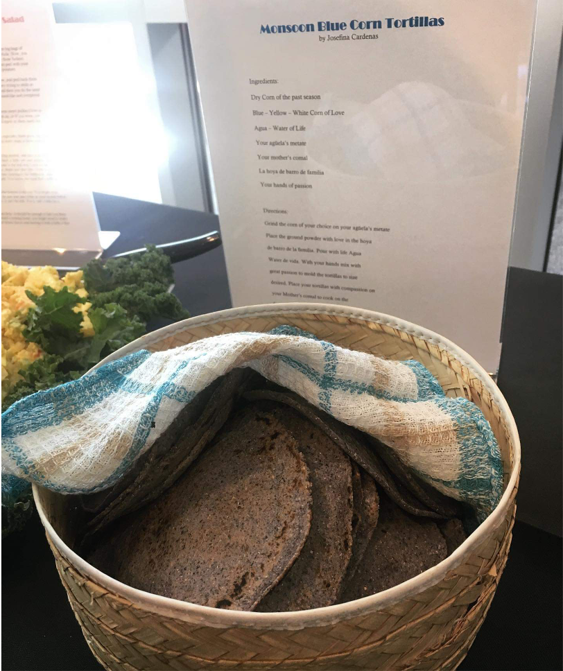 A basket with blue corn tortillas partially covered with a colorful cloth.