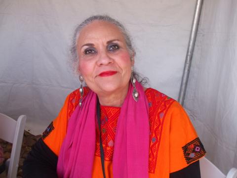 A woman sits in front of a white background in orange and pink clothes