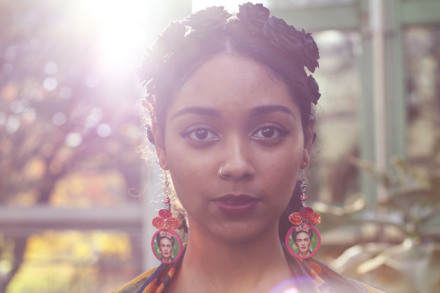 poet Safia Elhillo looks into the camera with rays of light bursting behind her