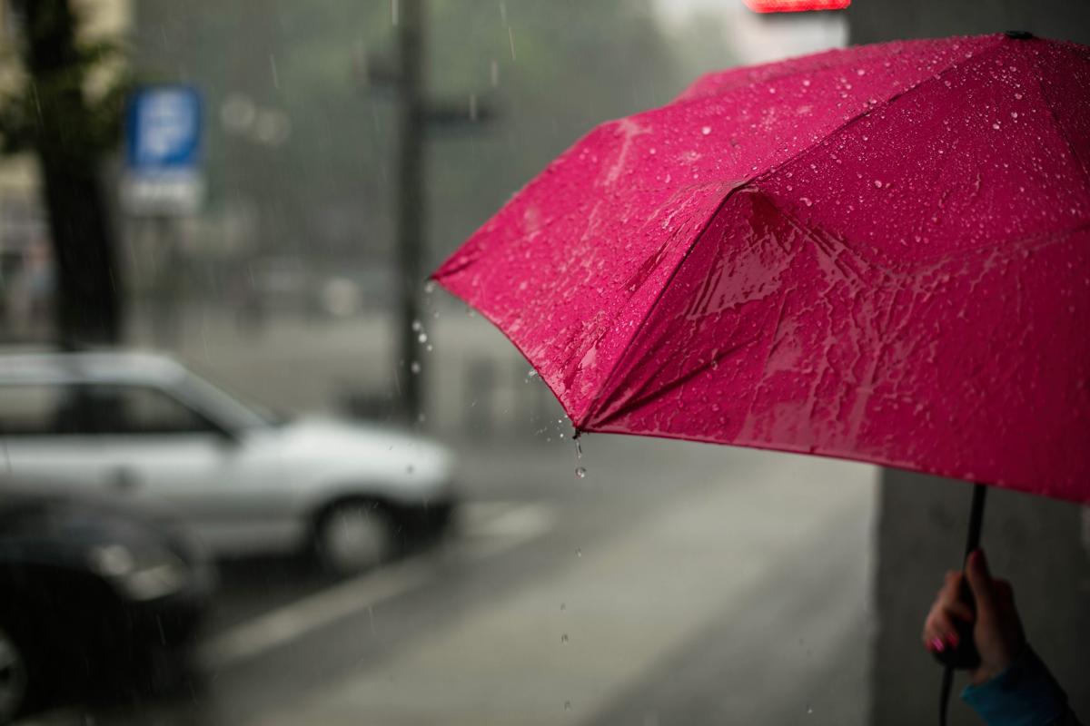 A hand holds a red umbrella on a city street in the rain