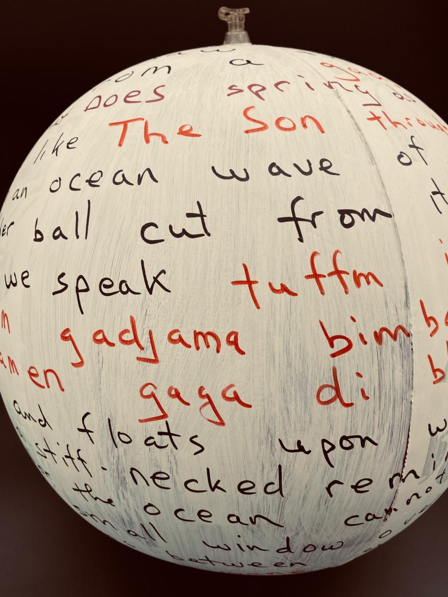 Photo of the Hugo Ball, an inflated beach ball covered in gesso, with text written on it in red and black permanent marker.