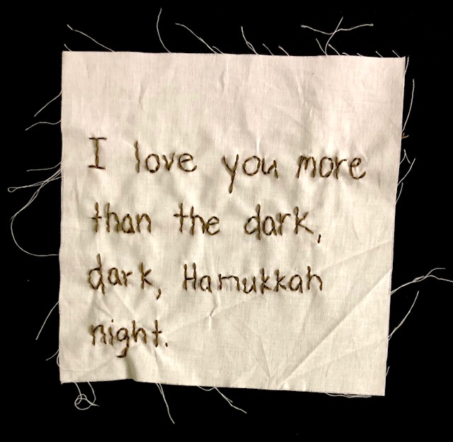 "I love you more than the dark, dark, Hannukkah night" stitched in brown thread on off-white canvas.