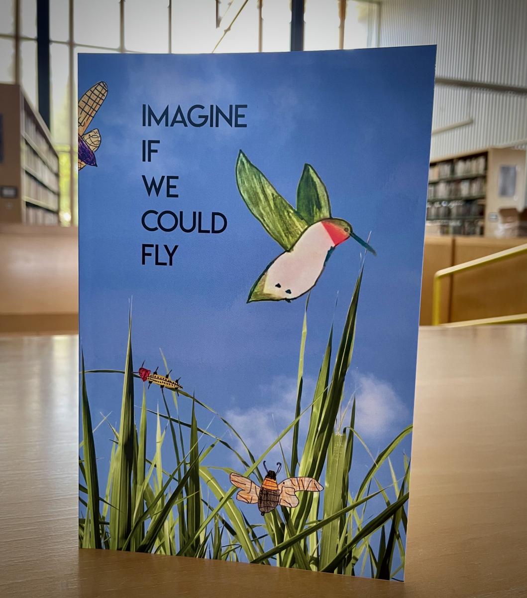 Book that reads "Imagine if we could fly" with a bird on it, grass, and a blue background