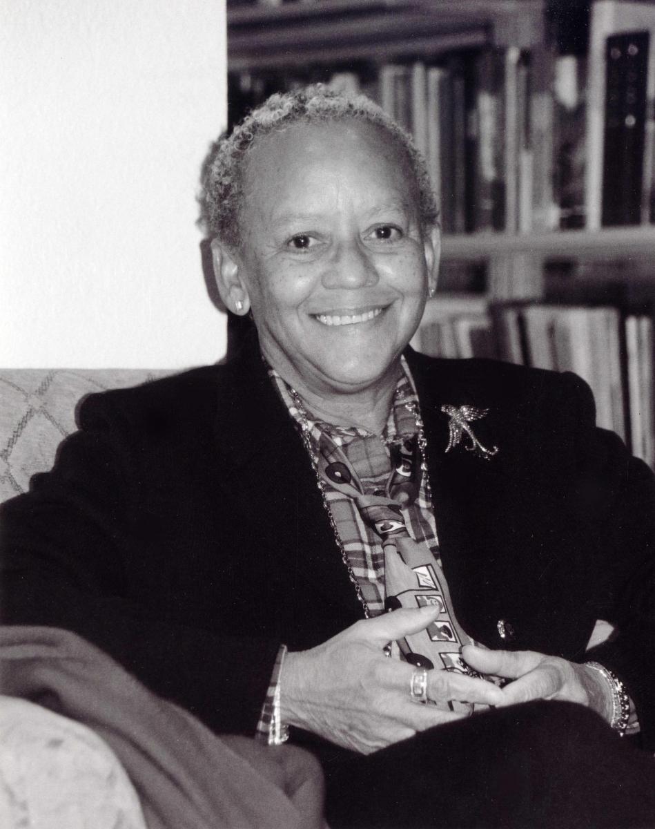 The poet sits in front of a bookshelf in a black blazer
