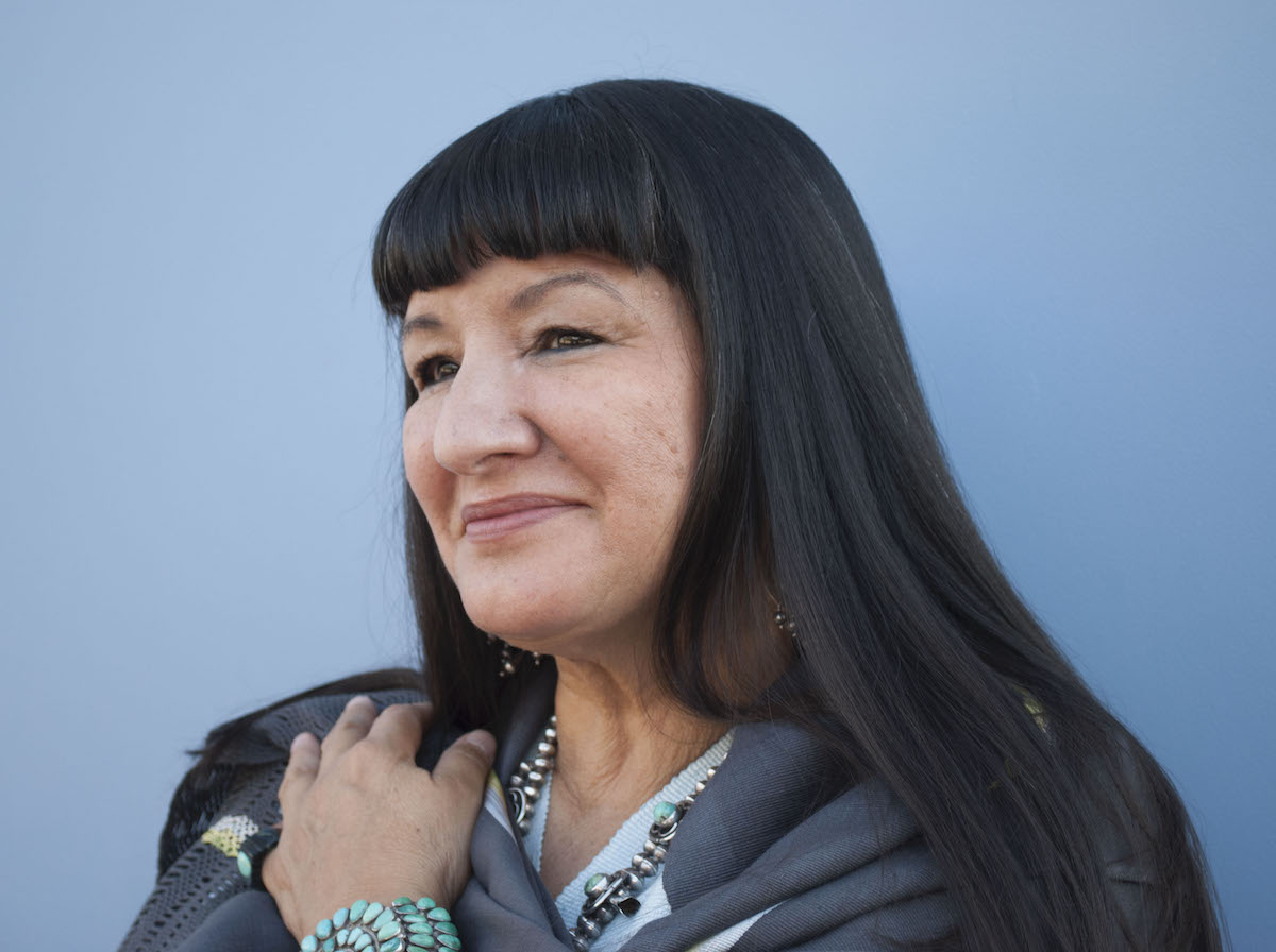 Sandra Cisneros looks off to the left standing against a blue background