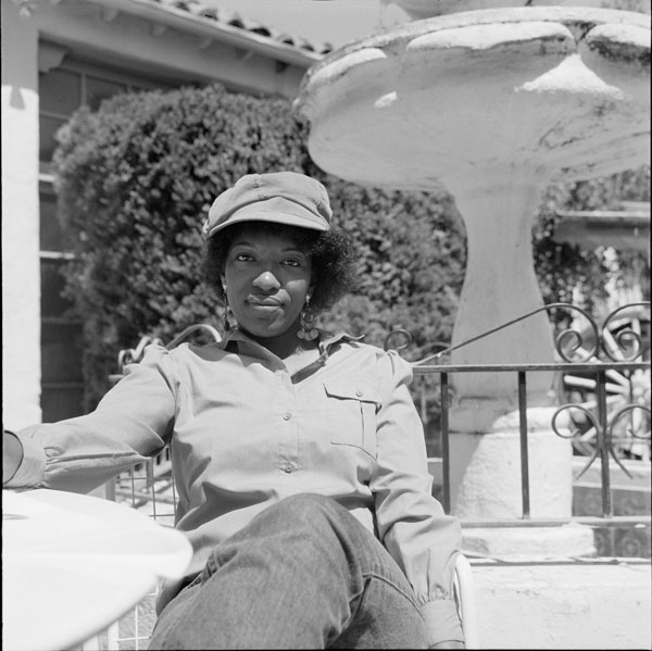 Poet Rita Dove wears a hat and sits by a fountain outside the Poetry Center.