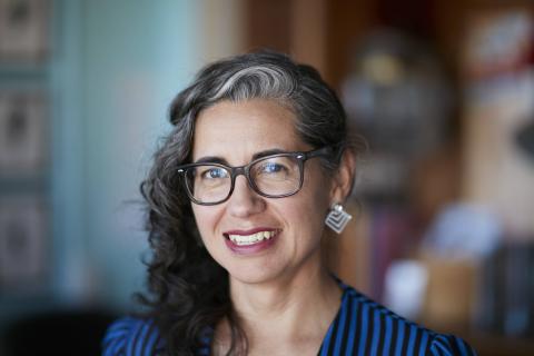 A woman with dark curly hair and glasses smiles