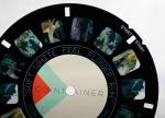 A black circle with small colored squares in grey, blue, green, and violet for use in a ViewMaster