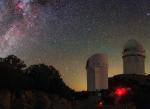 Two white, domed observatories sit on a ridge line with a starry night sky behind.