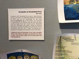 A label encouraging people to take home the colorful broadside displayed around the sign on a grey wall.
