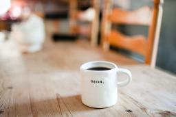 A white coffee mug with the word "Begin" on its side sitting on a wooden table.