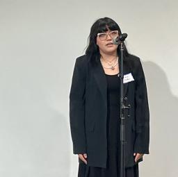 A student with long dark hair wearing all black talks into a microphone 