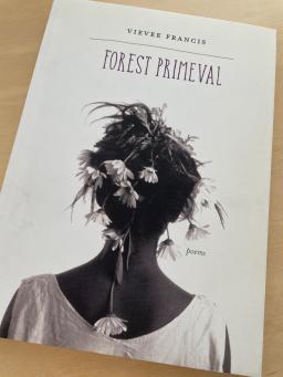 The cover of "Forest Primeval" by Vievee Francis, resting on a blond wood table.