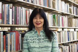 Joy Harjo stands in front of a full bookshelf at the Poetry Center