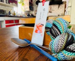 A color photograph of a spoon, a box, a bookmark, and some multicolored yarn.