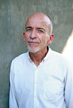 Mark Doty stands in front of a concrete wall at the Poetry Center, slightly smiling