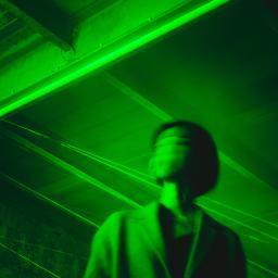 Person wearing coat with blurred face, in a parking structure, green filter. 