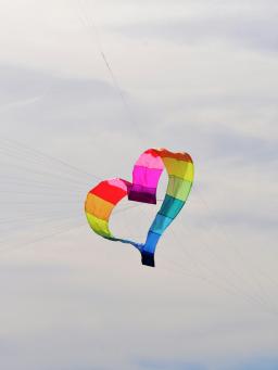 Heart shaped rainbow kite floats in a cloudy sky