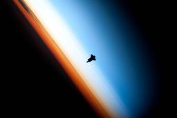 A space shuttler orbiter silhouetted against bands of black, orange, white, and blue.