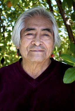 Simon J. Ortiz smiles at the camera, standing in front of a very green tree