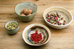 ceramic bowls of ingredients including cardamom, nutmeg, and rosebuds