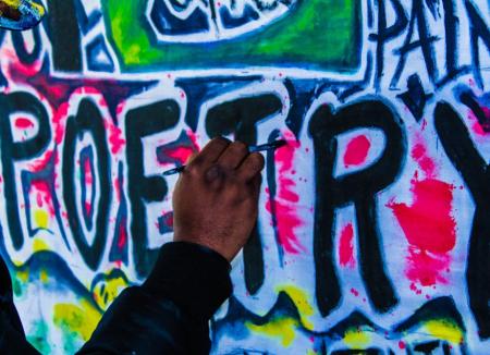 A hand adds pink paint to graffiti reading POETRY.