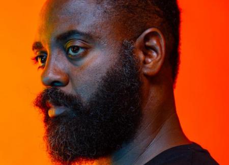 Reginald Dwayne Betts looks to the left agains a glowing orange background