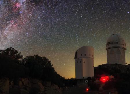 Two white, domed observatories sit on a ridge line with a starry night sky behind.