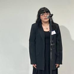 A student with long dark hair wearing all black talks into a microphone 